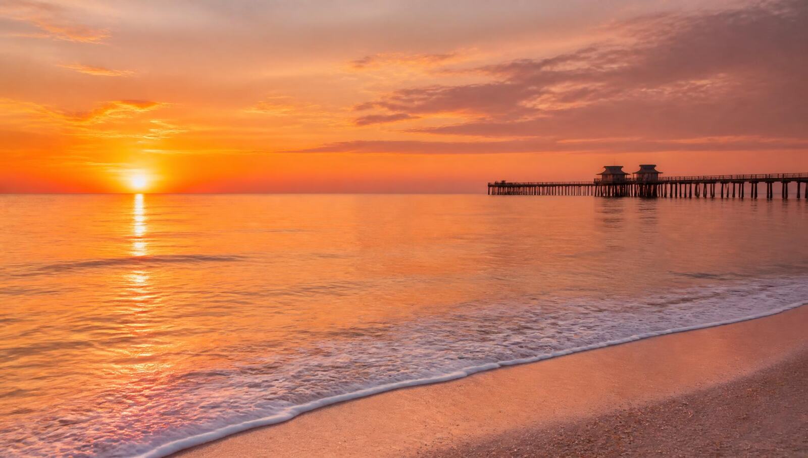 Sunset over the Gulf of Mexico with the Naples Pier silhouetted against orange sky