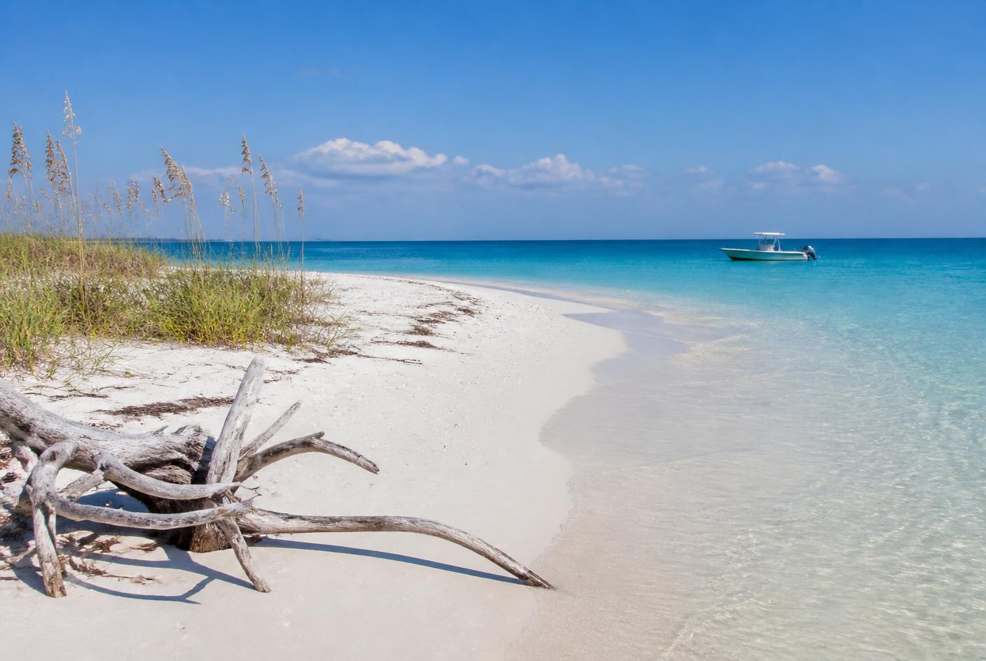 Undeveloped white sand island beach with clear shallow water and a boat anchored offshore